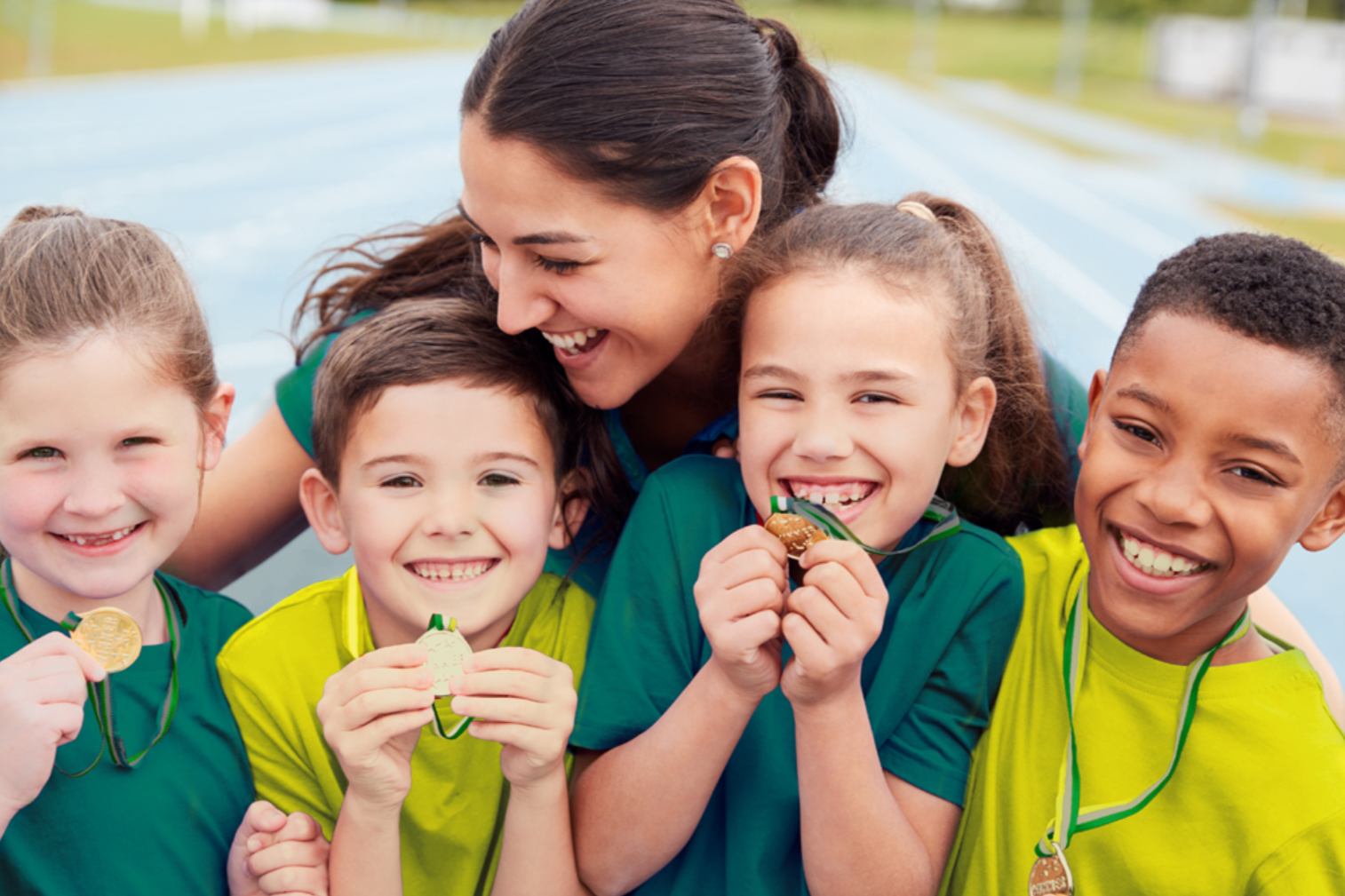 Four children dressed in green and gold holding medals with a coach