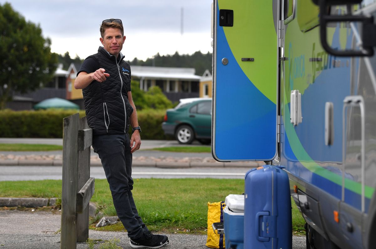 Gene Bates stands next to cycling van pointing at camera.